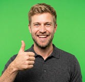 Smiling man with short blond hair giving a thumbs-up against a bright green background while wearing a dark polo shirt.